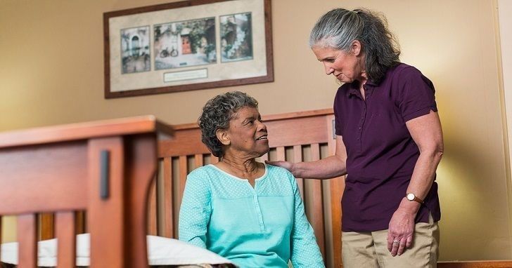 home instead caregiver standing beside senior sitting on the edge of the bed at home