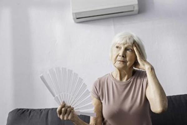 Older woman sitting inside fanning herself.