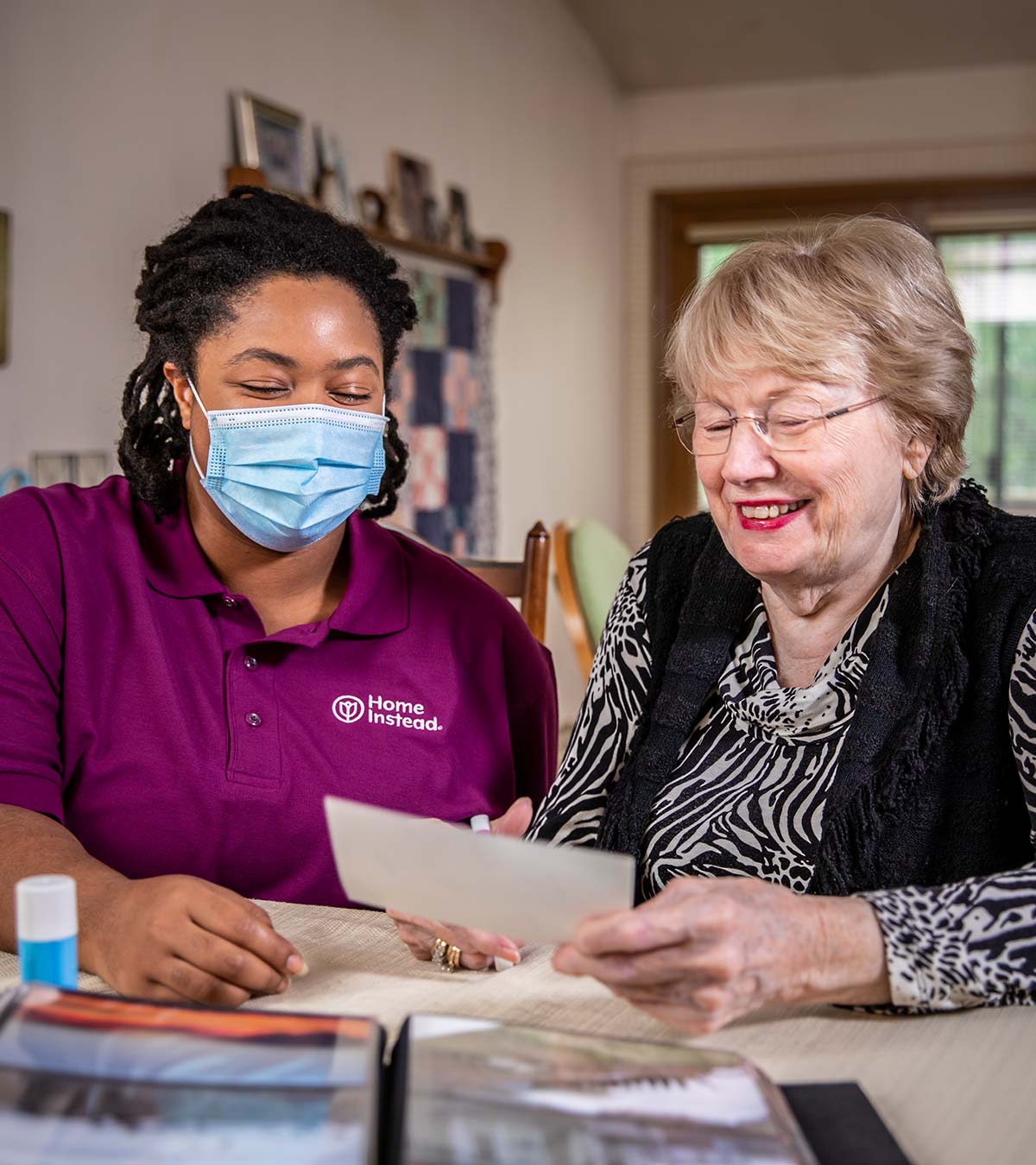 A masked caregiver keeping company to a senior at her home