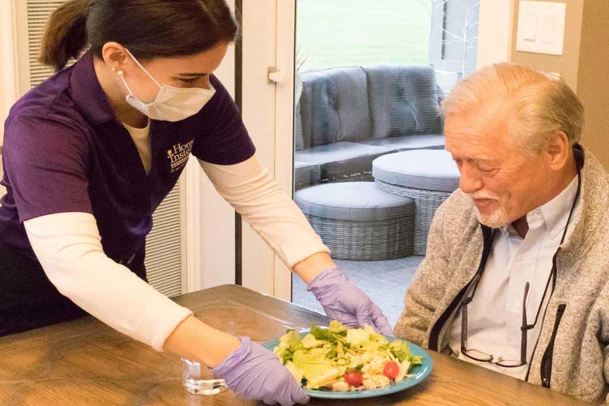 Masked Caregiver serving dinner to a senior