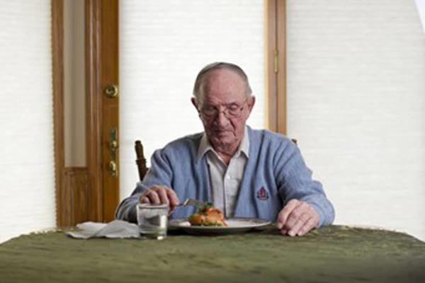 Elderly man sits alone at a table eating food.