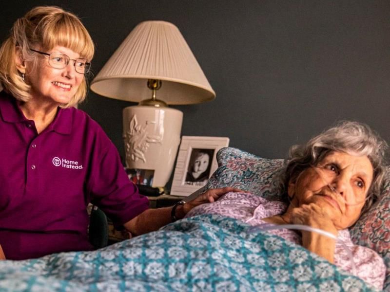 home instead caregiver comforting senior client laying in bed