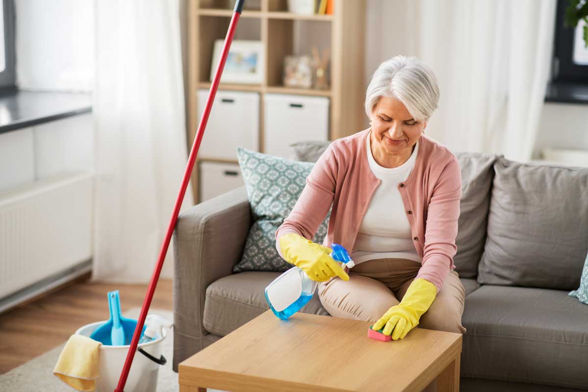 A senior seating while using cleaning products  to clean coffee table