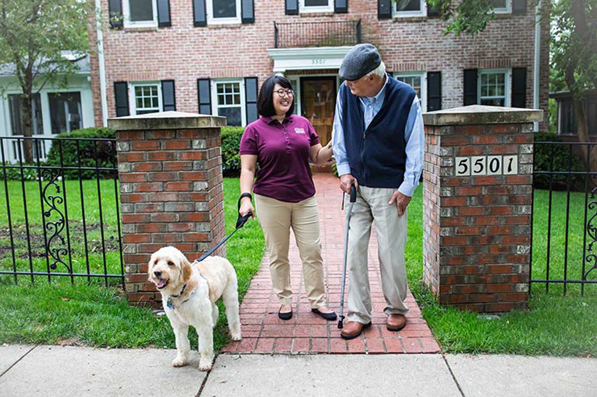 Caregiver and senior going for a stroll while taking the dog for a walk