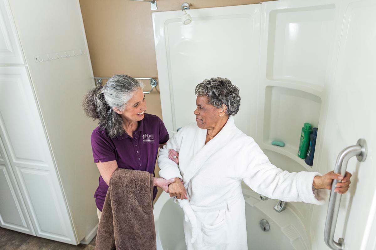 A Home Instead Caregiver helps a senior to enter safely into the shower to avoid falls