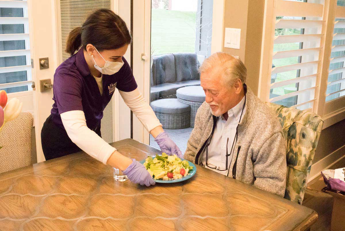 A Home Instead Caregiver serving dinner to a senior.