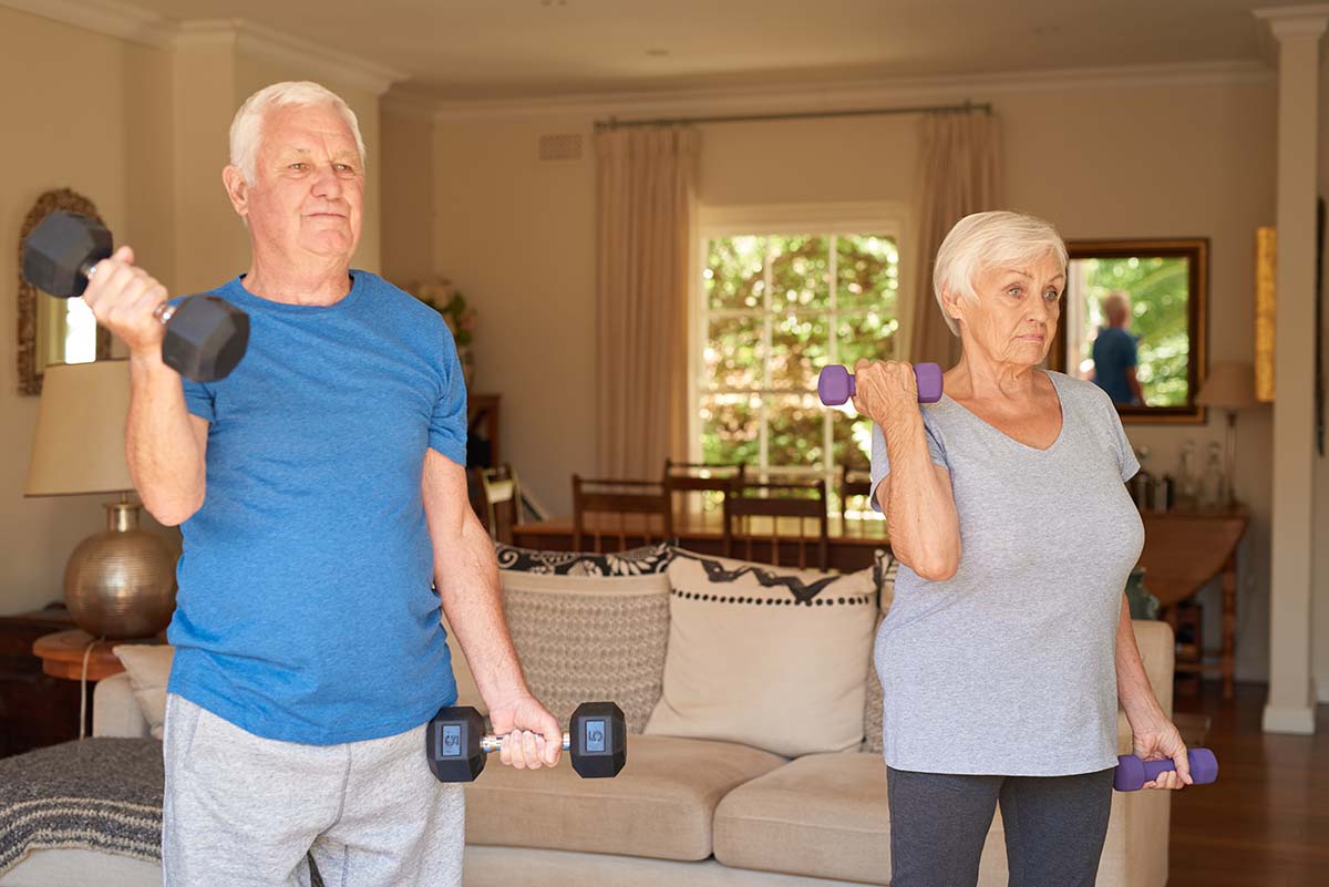 Active couple lifting dumbells together in their living room