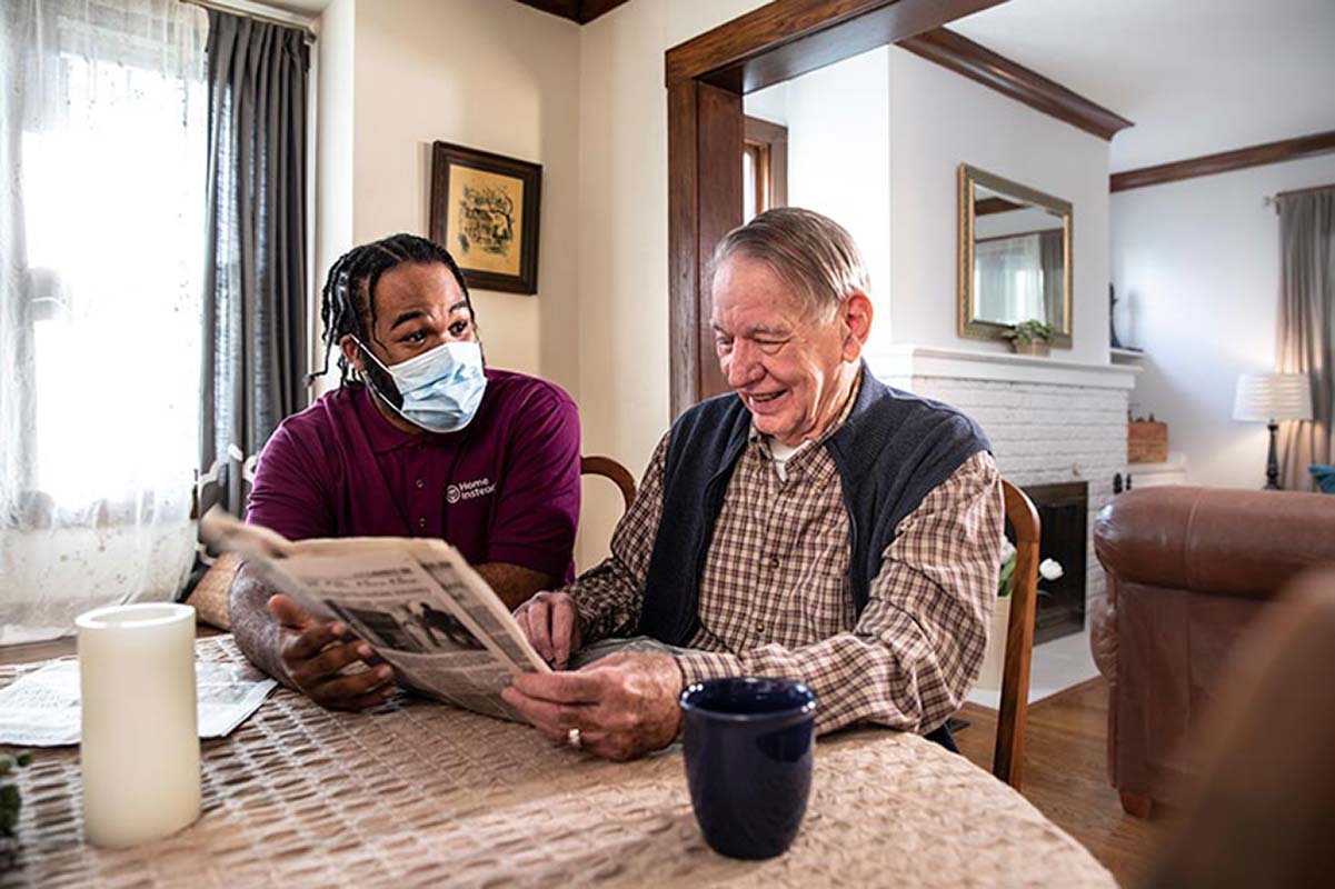 A senior is reading the newspaper and commenting the news with a Home Instead CAREGiver