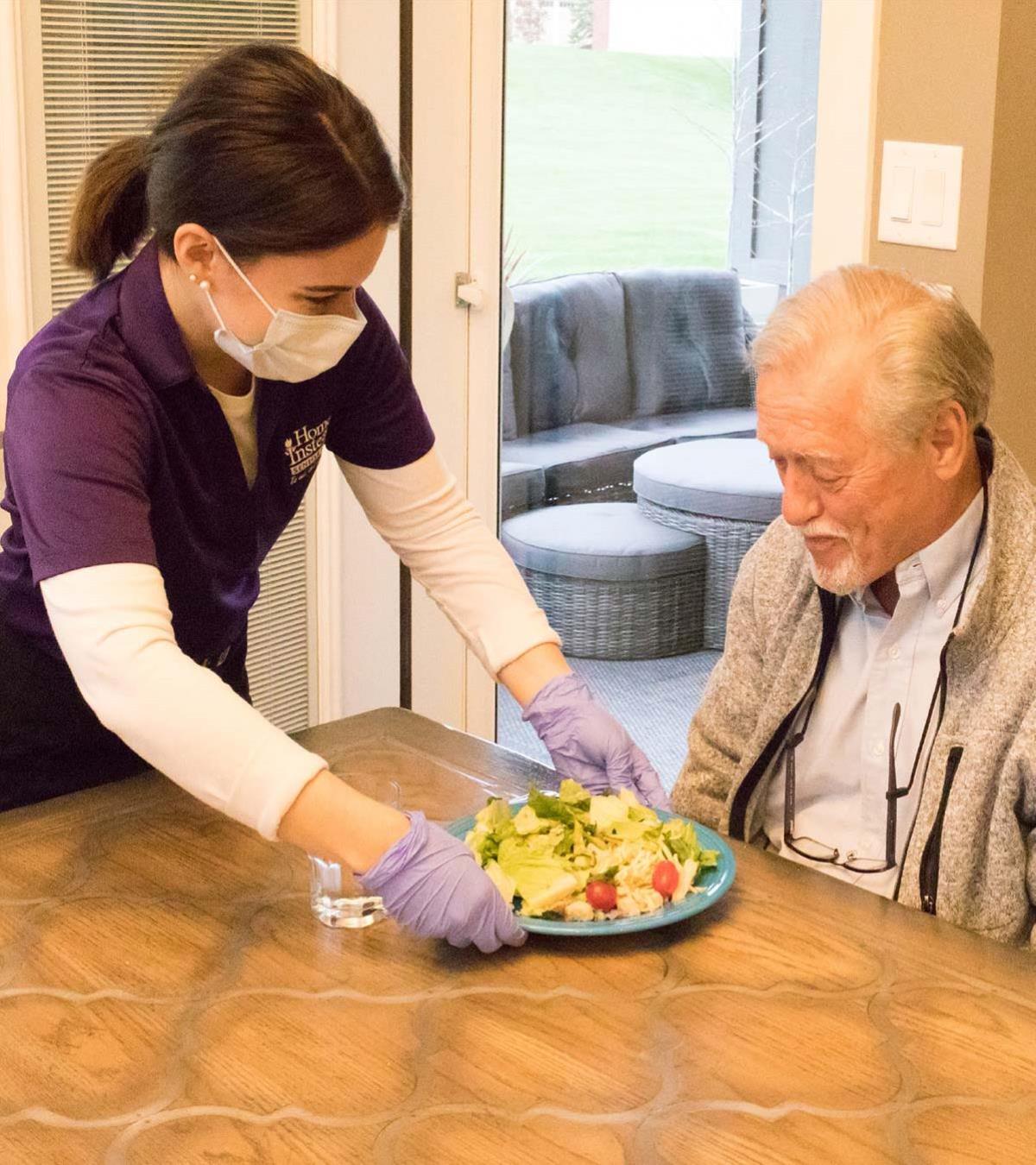 masked caregiver serving dinner to a senior