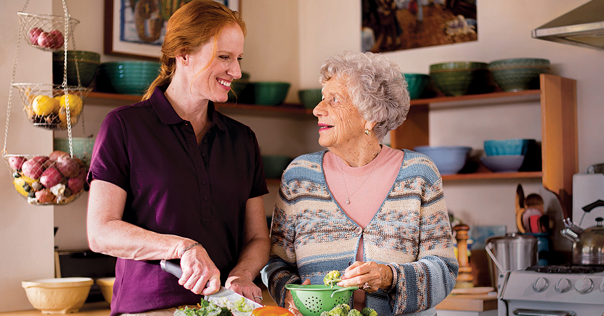 A Home Instead CAREGiver smiling with senior on the couch