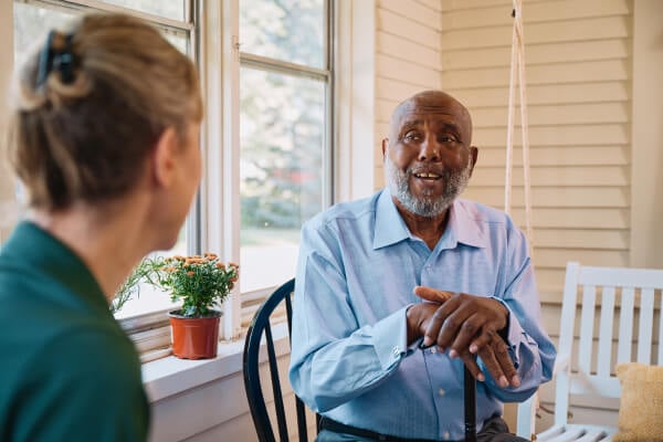 Home caregiver smiles and chats with an older gentleman in his living room.