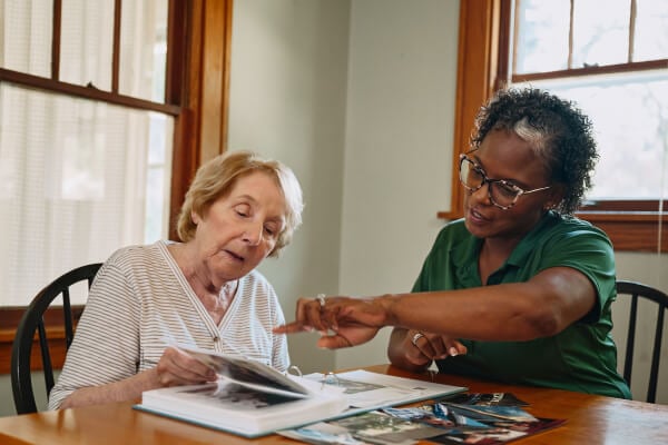 Care professional and older adult reminiscing over a photo album.