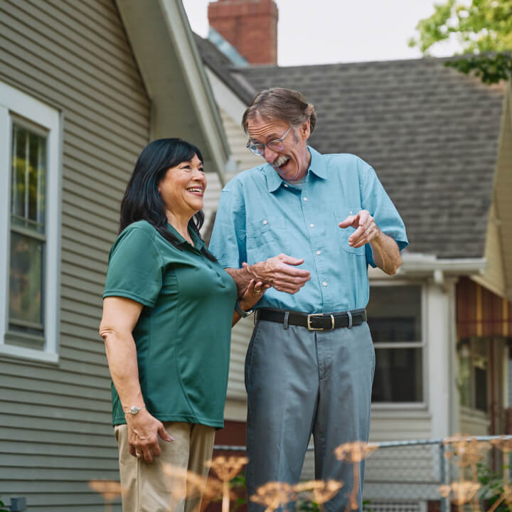 A Home Instead caregiver walks outdoors with an elderly man, both laughing and enjoying the fresh air, representing active engagement and companionship.