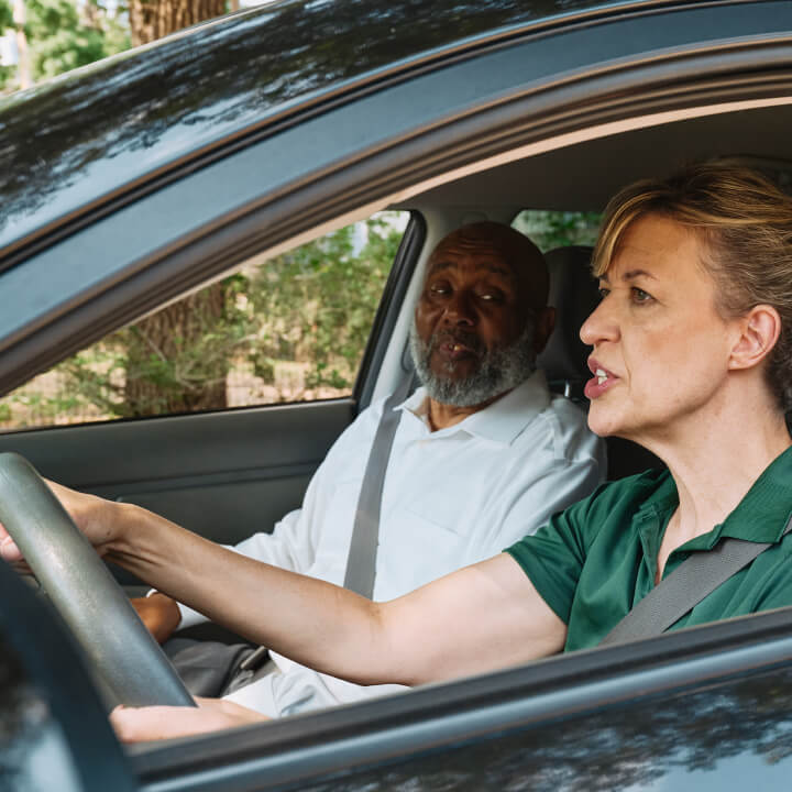 A Home Instead caregiver assists an elderly man in the passenger seat of a car, preparing for a safe and comfortable ride, showcasing reliable transportation support.