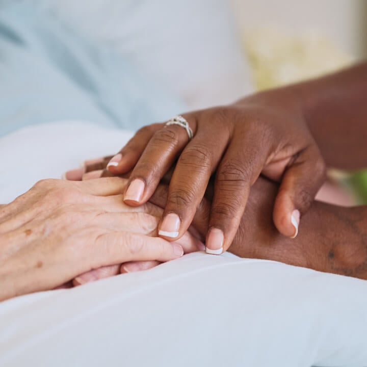 A close-up of a Home Instead caregiver's hands gently holding the hands of an older adult, showcasing compassion, trust, and care.