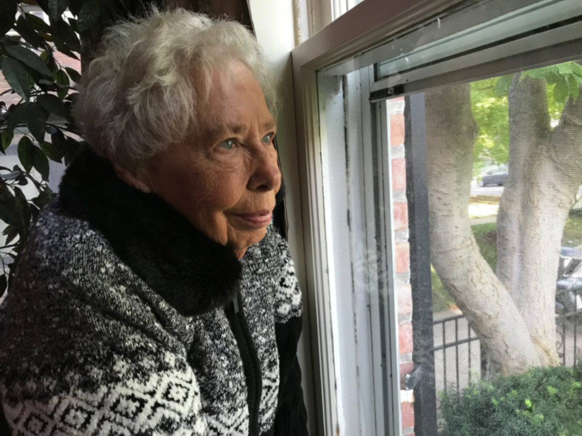 Elderly woman gazes out the window of her home.
