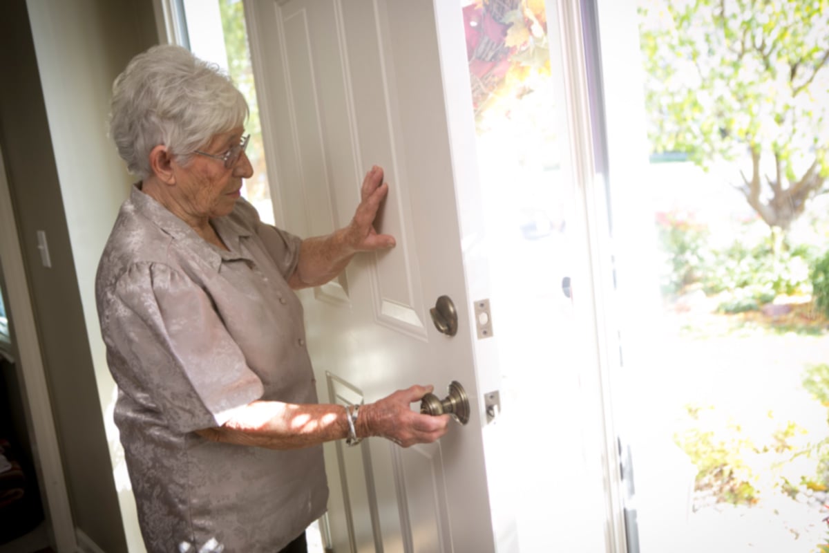 Senior woman with delusions caused by dementia opens the front door of her home