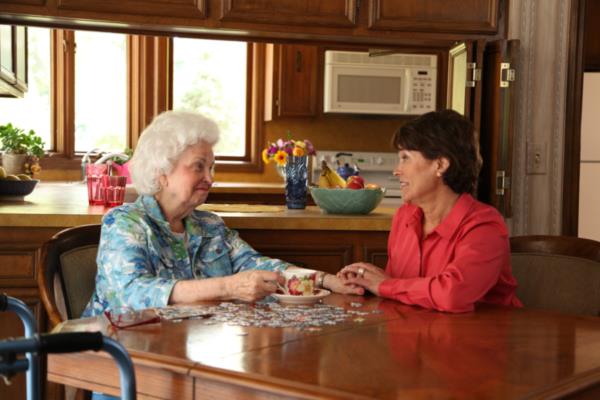 Senior woman and daughter sit talking at the kitchen table at home