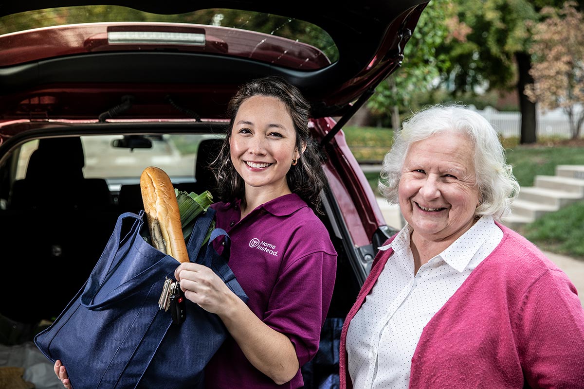 Home Instead Caregiver helps senior woman unload groceries from vehicle
