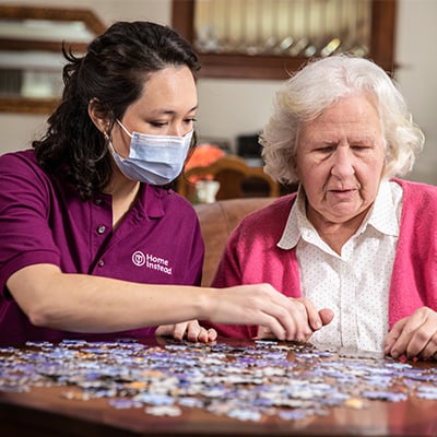 Home Instead Caregiver wearing mask and senior woman work on puzzle at home