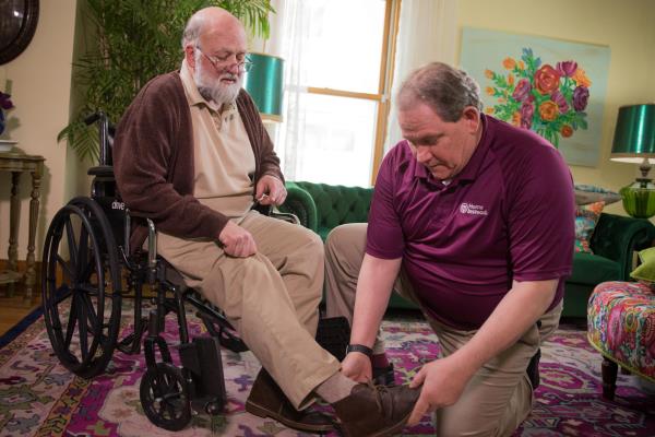 Caregiver helping senior in a wheelchair put on his shoes